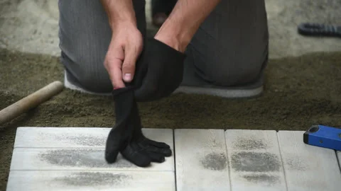 Man putting on work gloves before laying paving slabs Stock Footage 242405977