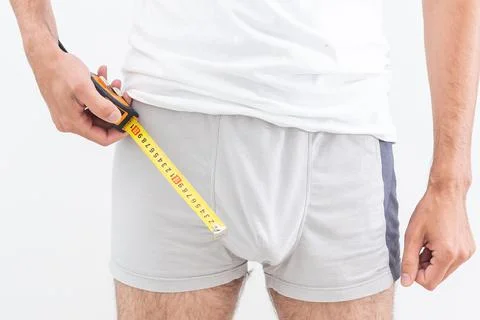 A man questioningly holds a measuring tape to his underpants. Stock Photos