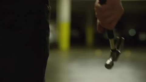 A man quickly aggressively walks through a car parking with a hammer in his hand Stock Footage 194021647