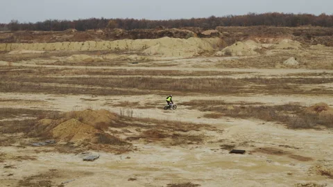 Man on a racing motorcycle rides on sandy off road and jumps across small hill. Vidéo 142093183