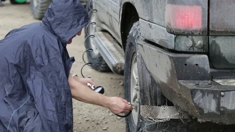 Man in raincoat pumping wheels of SUV at roadside Stock Footage 76261621