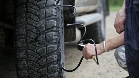 Man in raincoat pumping wheels of SUV at roadside Stock Footage 76262089