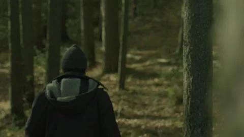 A man in a raincoat walks through the forest between tree pillars. Stock Footage 273708378