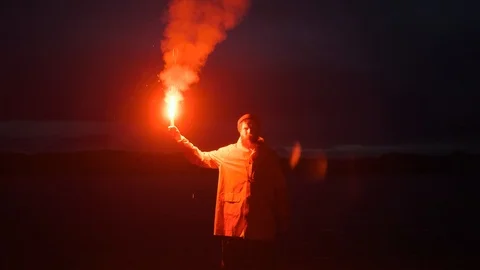 Man raincoat,waving red smoke signal,light, lake mountains.traveler night Stock Footage 126315341