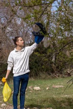Man with a raised hand picking up garbage bag hooked on windblown tree Stockfoto's