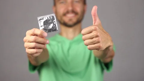 Man raises in front of him on right outstretched hand condom, gesture thumb up Stockbeeldmateriaal 94926806