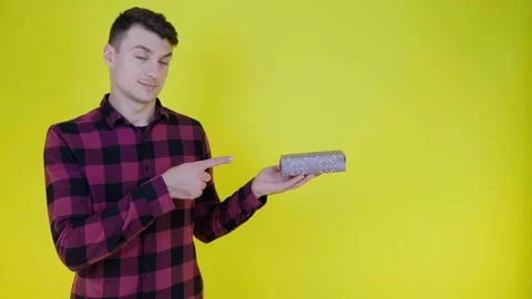 Man raises hand and points finger at box with gift in palm on yellow background Stock Footage 134233881