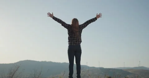 Man raises hands up standing back on mountain top morning sun shine. Achievement Stock Footage 195245890