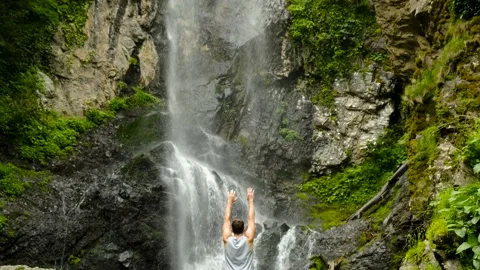 A man raises his hands up against the background of the Mervisi waterfall in Stock Footage 198659402
