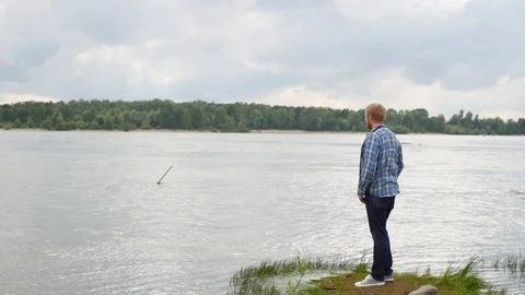 Man raises his hands standing by the river. a man stands with his back and looks Stock-Footage 107180860