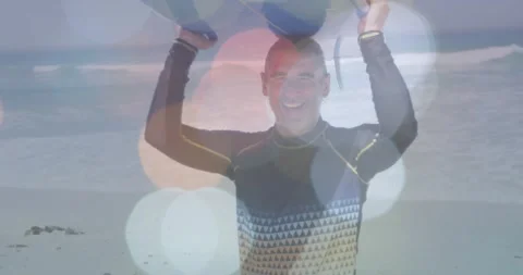 Man raising blue board on beach, posing for surf promo while bokeh overlays 스톡 동영상 329752629
