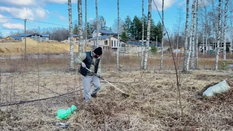 A man raking dry grass in spring at his country plot Vídeos de archivo 306574689