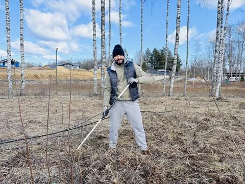 A man raking dry grass in spring at his country plot Stock Photos