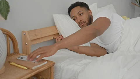 Man reaching with hand for smartphone on bedside table in bedroom with whit.. Stock Footage 337440368