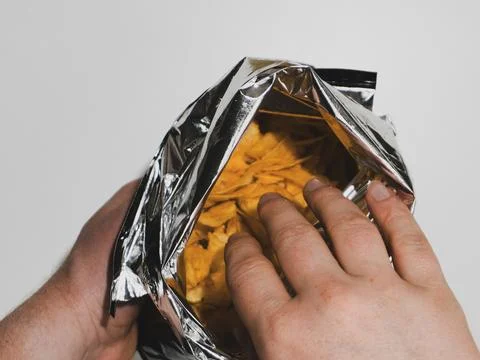 Man reaching into an open silver foil bag of potato chips Foto stock