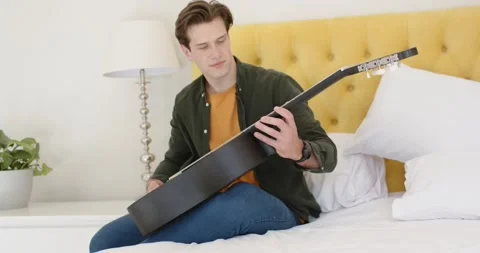 Man reaching, pulling black acoustic guitar onto lap, tuning strings and testing 库存影片 347459329