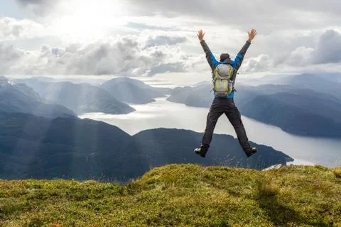 Man reaching summit and leaping for joy. Stunning view to coastal mountains and Stock-Fotos