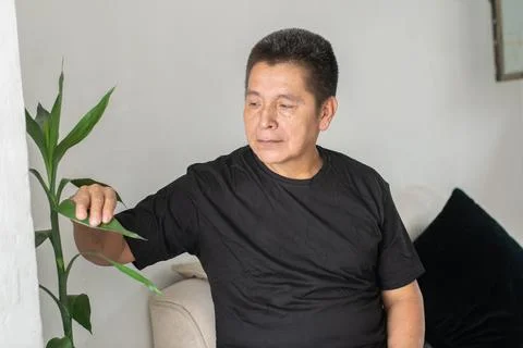 Man reaching toward plant while sitting on couch showing simple home activi.. Фото