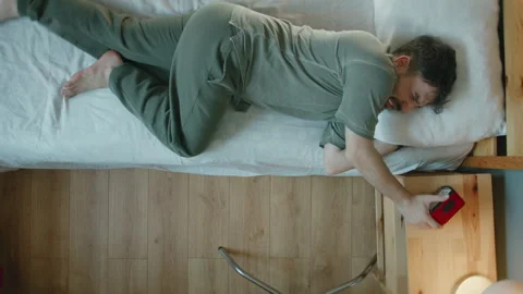 Man reaching to turn off alarm clock in bed, early morning wake up struggle Stock Footage 344109370