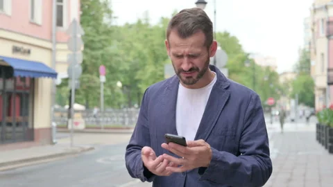 Man Reacting to Loss on Phone while Walking Down the Street Stock Footage 158369786