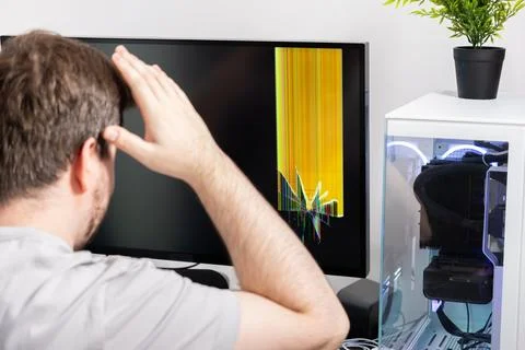 Man reacts with dismay to a broken computer monitor displaying vivid colore.. 스톡 사진