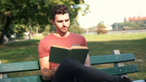 Man reading absorbing book and sitting on the bench in the park Stock Footage 69964419