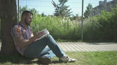 Man reading aloud book under tree, pan shot. 動画素材 52689427