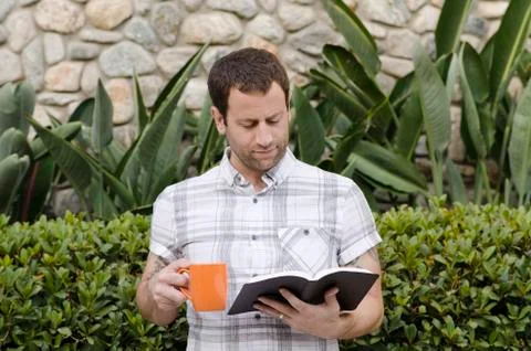 Man reading the Bible while holding an orange coffee mug. Stock Photos