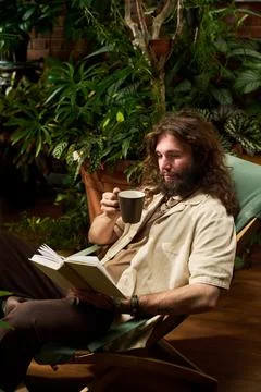 Man Reading Book and Drinking Coffee in Indoor Garden Fotos de archivo