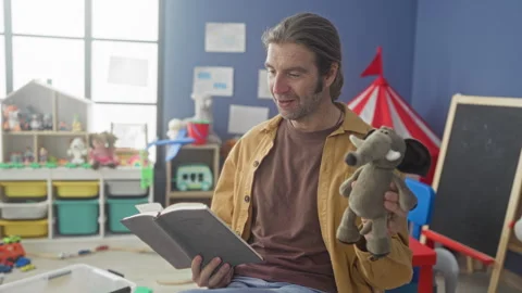 Man reading book and holding stuffed elephant with hand in preschool playro.. Stock Footage 339191693