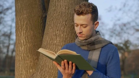 Man reading book and smiling to the camera in the park, steadycam shot Vídeos de archivo 70757165