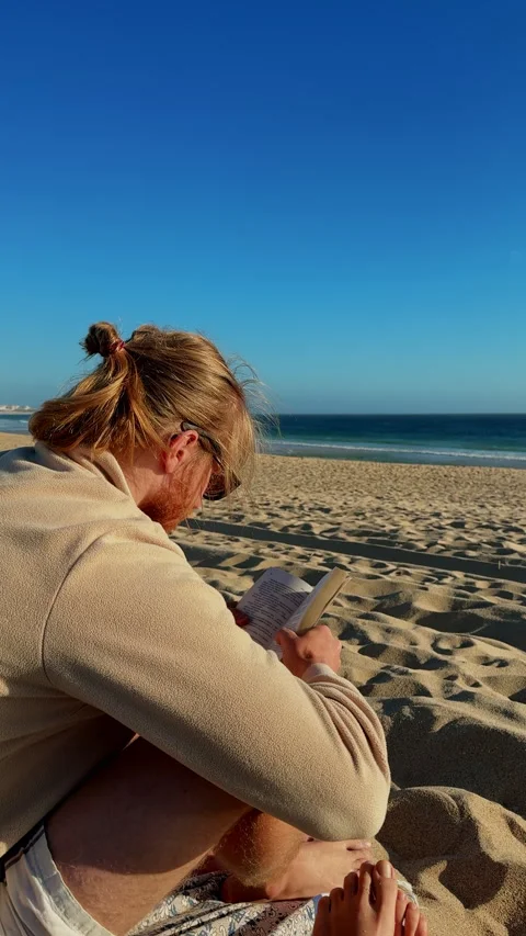 Man reading book on Baleal beach overlooking Atlantic Ocean Vídeo Stock 339222392