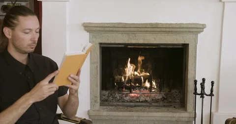 Man reading a book by the fireplace 動画素材 97974152