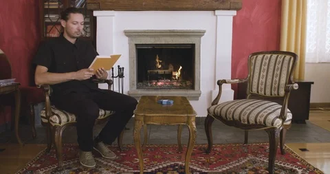 Man reading a book in front of a fireplace Vídeo Stock 97974100