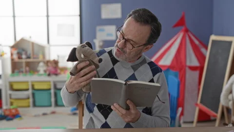 Man reading book holds elephant puppet in school building reading aloud at .. 스톡 동영상 337445038