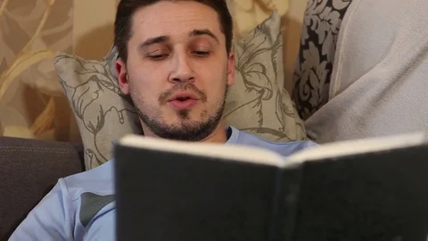 Man reading a book lying on the couch Stock Footage 72580579