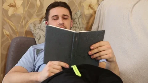 Man reading a book lying on the couch and dreams Stock Footage 72580961
