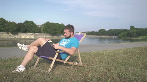 Man is reading book, lying on sunbed by the river. Vidéo 65205685