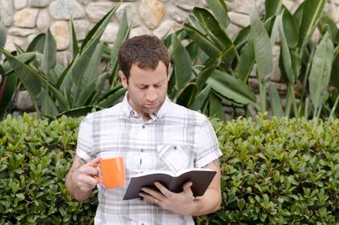 Man reading a book outdoors while holding a coffee mug. Stock Photos