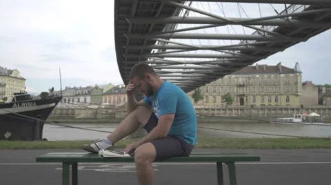 Man is reading book, sitting on bench against the river. Vídeos de archivo 65188215