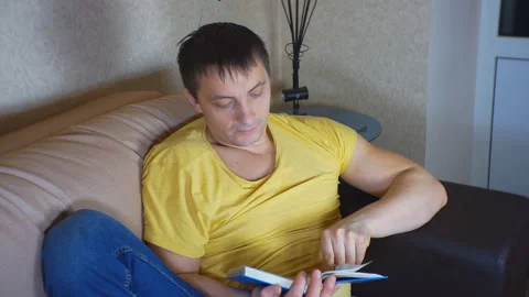 Man reading a book sitting on the couch. Stock Footage 103371767