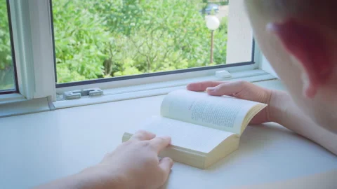 Man reading a book sitting at an open window on a sunny day, back view Stock Footage 195010464
