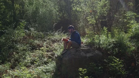 Man reading a book sitting on a rock in the middle of the forest. Stock Footage 139613096