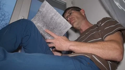 A man reading a book sitting on a windowsill. Stock Footage 97784409