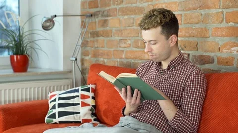 Man reading book on the sofa and smiling to the camera, steadycam shot Stock-Footage 70852512