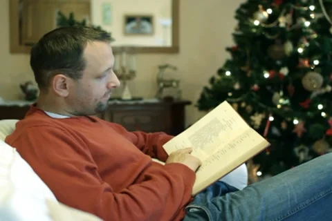 Man reading book on sofa, christmas tree in background Stock Footage 10741984