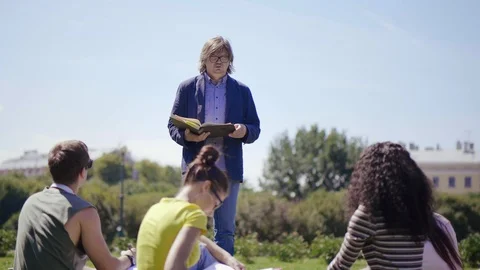Man reading book to students in the park. Stock Footage 93132925