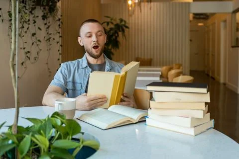 Man reading book at a table filled with study materials in a modern learnin.. Photos