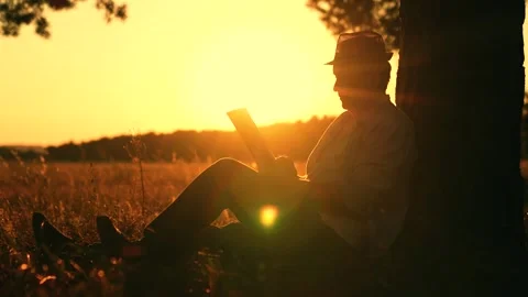 Man reading book with tablet under tree in park, thinking relaxing in nature Stock Footage 315910758