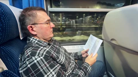 Man Reading a Book on a Train During Evening Travel 스톡 동영상 297702802